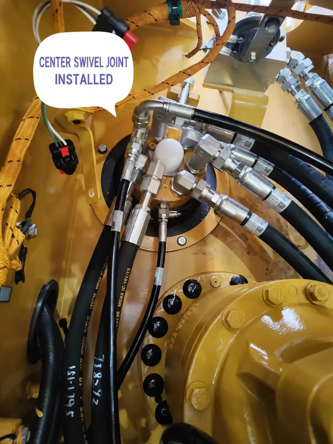 Center swivel joint fitted inside the excavator with hydraulic hoses and metal fittings connected.
