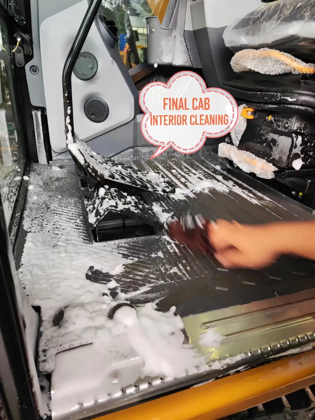 Cleaning the excavator cab floor with foam and a brush.
