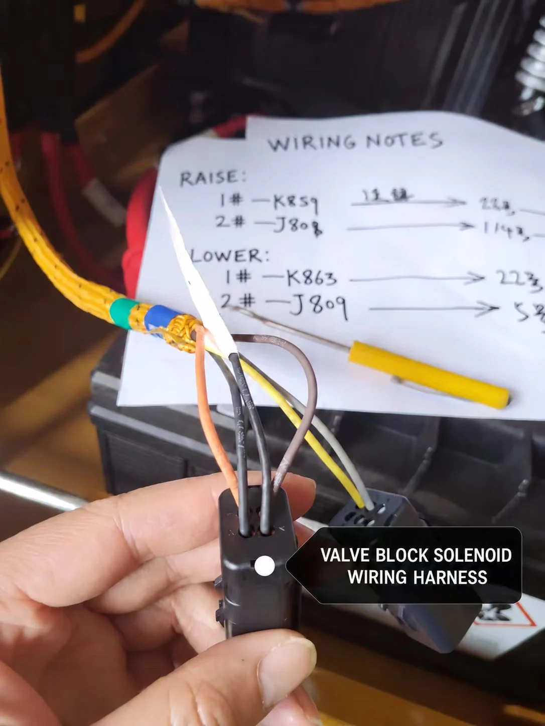 Three-wire valve solenoid connector held beside handwritten project wiring notes.