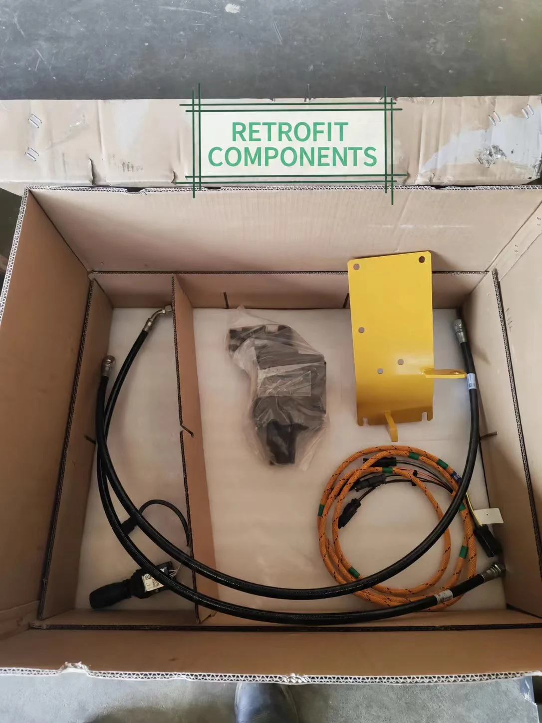 Box of excavator retrofit components containing hoses, wiring and a mounting plate.